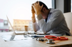Physician holding head in hands due to burnout