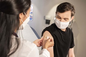 female practitioner putting a Band-Aid on injection site of young mans arm