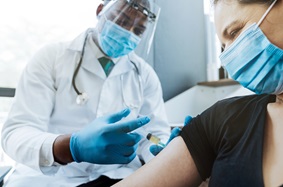Healthcare worker injecting vaccine on female patient's arm at medical clinic. Scared woman looking at COVID-19 antidote injection.