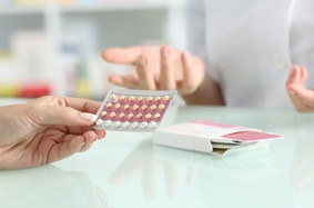 person holding birth control pills while sitting across from another person