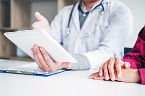 A doctor explaining a medical procedure to a patient while holding a computer tablet