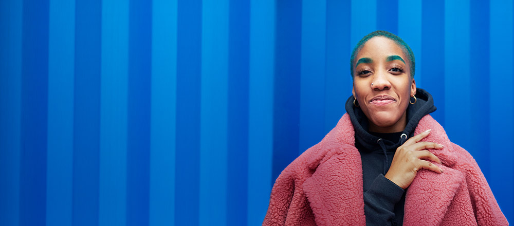 Woman smiling and looking confidently into the camera while wearing a pink coat on a blue background