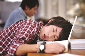 man asleep on laptop on top of desk