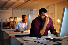 A stressed man holding his head while working late at his office computer