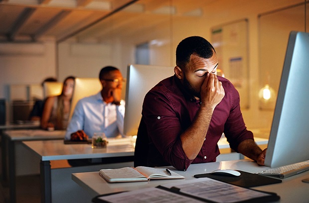 A stressed man holding his head while working late at his office computer