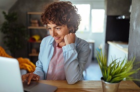 Middle-ages woman scrolling through her laptop in her home