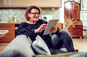 A middle aged woman sitting on the couch looking at an digital tablet