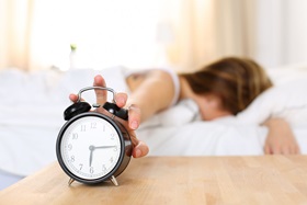 Tired woman in bed ignoring the alarm clock.