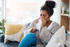 young woman sitting on a couch and blowing her nose