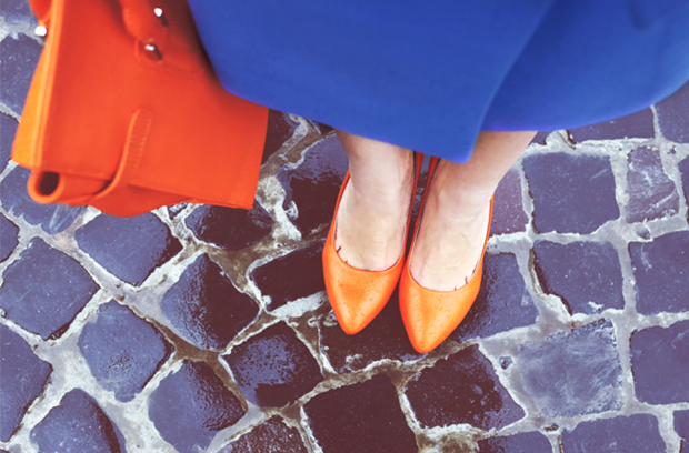 woman_stands_on_stone_road_wearing_orange_plastic_dress_shoes_and_blue_dress_carrying_red_bag_in_rain