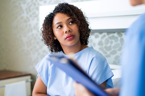 Young woman sitting on hospital bed listening to doctor