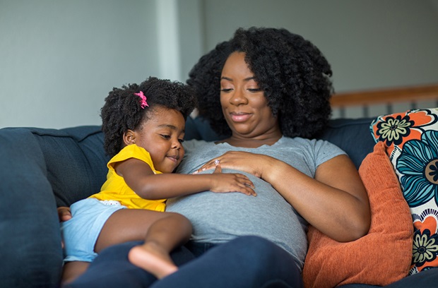 A pregnant mother and her young child sitting on a sofa smiling