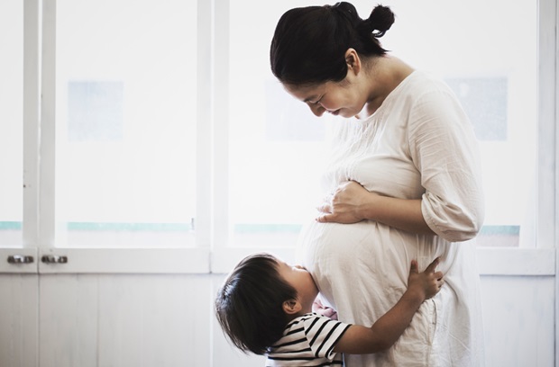 Toddler hugging and kissing pregnant mother's belly