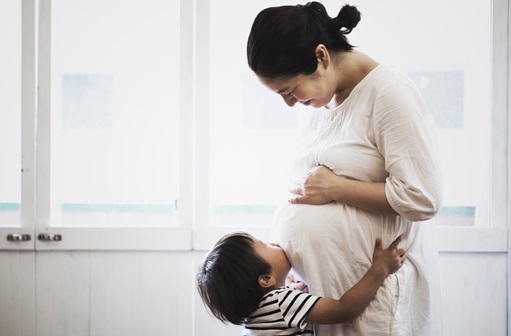 Toddler hugging and kissing pregnant mother's belly
