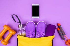 Hand weights, a water bottle, sneakers, a jump rope and a smartphone arranged in a semi-circle