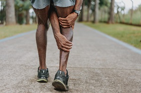 Man in sneakers and shorts holding his right leg in pain