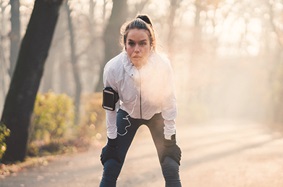 young woman stops by tree to catch breath during run