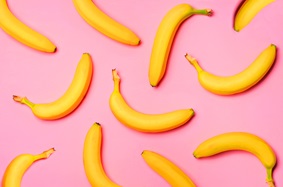 11 unpeeled loose bananas arranged on a pink background