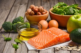 a table with salmon, eggs, broccoli, spinach, nuts, avocado and an apple on it