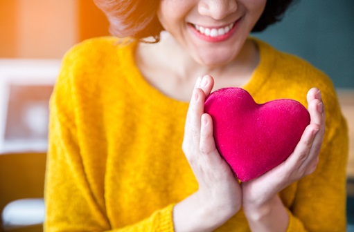 Woman wearing gold sweater holding stuffed red heart. 