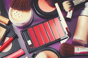 open palette of lipgloss with brush, bronzer, foundation, loose powder foundation, lipstick, highlighter, and lip liner lay out on a purple table