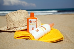 Sunscreen SPF 50, straw hat and towel on beach