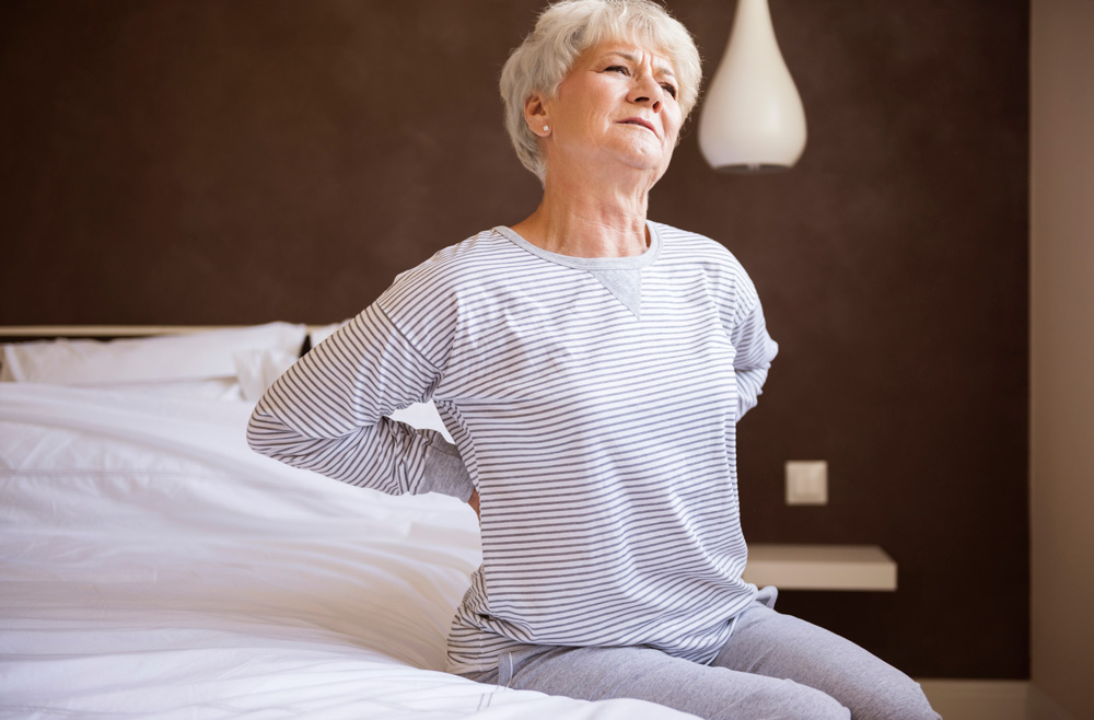 woman holding back in pain while sitting in bed