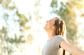 woman smiling with her arms outstretched with trees in the background