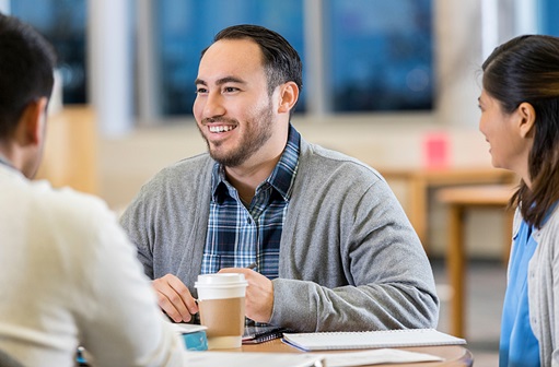 Young-adult man smiling while talking to a group of people.