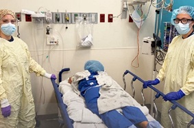Two Penn nurses in scrubs show a patient in the prone position in a hospital bed