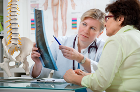 middle aged female doctor looks at x-ray of spine next to diagram of spine with a senior female patient. 