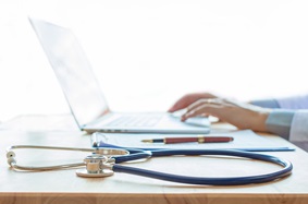 hands typing on laptop with a stethoscope next to it