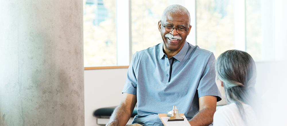 Older man smiling facing doctor with clipboard