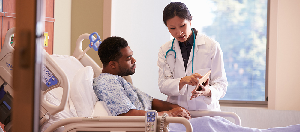 Female doctor speaking to male patient who is in bed
